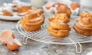 Färska petit choux på ett galler, med äggskal i förgrunden. Perfekt för en fika!