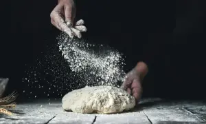 Händer strör mjöl över en deg. Det ser ut som en svensk hemmabakare som förbereder sitt bröd med fint **bread flour svenska**.