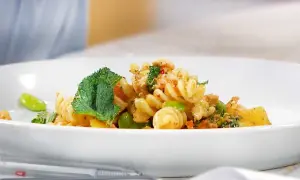 En läcker pastasallad med kyckling, gröna bönor och mynta på en vit tallrik.