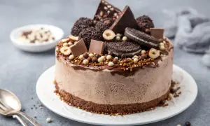 En chokladglassbakelse dekorerad med chokladbitar, oreos, hasselnötter och strössel. Enkel chokladsås rinner ner längs sidorna.