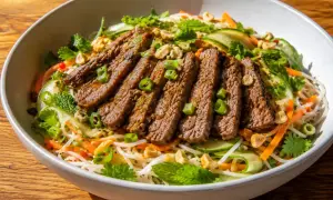 En skål med asiatisk biffsallad med nudlar, strimlad biff, gurka, morötter, mynta och jordnötter.