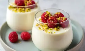 Två glas med len pannacotta vit choklad, toppade med hallon och pistagenötter. En dröm för smaklökarna!
