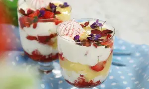 Två glas med Eton Mess, lager av vispad grädde, jordgubbar och maräng, toppade med blommor.