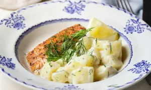 En bit lax med dill och en krämig stuvad potatis, serverad på en vacker blåvit tallrik.