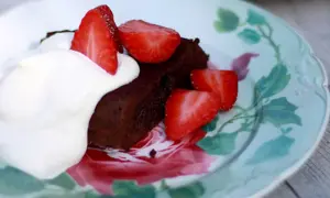 En bit fransk chokladtårta med vispgrädde och färska jordgubbar på en vacker tallrik med blomstermönster.