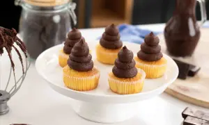 Fem cupcakes med fluffig chokladganache på en vit tårtfat. Ingredienser för chokladganache syns i bakgrunden.