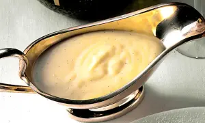Krämig vaniljsås med små prickar av vaniljsocker i en elegant silverkanna, redo att serveras.