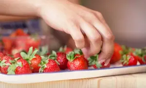 En hand plockar bland färska jordgubbar på ett fat, redo att läggas i kylskåpet för att bevara deras sötma.