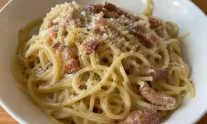 En skål med krämig pasta carbonara, toppad med parmesan och svartpeppar.
