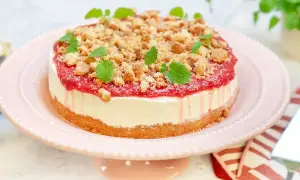 En krämig rabarber cheesecake med smulig topping och färska myntablad, serverad på ett rosa tårtfat.