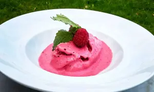 Hallonglass, gjord i en glassmaskin, serveras i en vit skål med färska hallon och mynta.