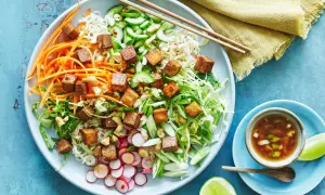 En färgglad asiatisk nudelsallad med krispiga grönsaker, cashewnötter och gyllene tofu-kuber. Serveras med en dressing och limeklyftor.