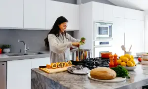 Kvinna lagar mat i ett modernt kök. Frukt, bröd och grönsaker ligger på bänken, bra spartips mat.