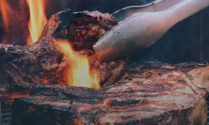 En saftig entrecote grillas över öppen eld, perfekt innertemp. Tången vänder köttet för en jämn stekyta.