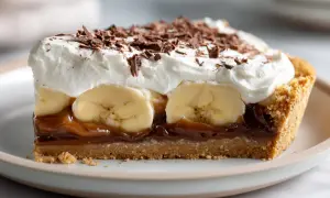 En bit krämig banoffee paj med banan, kolasås, vispgrädde och chokladströssel.