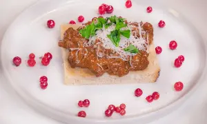 En läcker svampstuvning på kantareller serveras på rostat bröd, toppad med riven ost och färska örter. Runt tallriken sprids röda lingon.