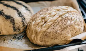 Två rågbröd med flätat mönster och sesamfrön, redo att bakas. Glutenrik njutning väntar!