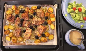 En härlig mat på plåt med köttbitar, potatis, fänkål och plommon. Bredvid en sallad och en skål med sås.