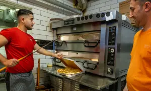 Två pizzabagare jobbar vid en stor pizzaugn. En tar ut en färdig pizza i Sverige.
