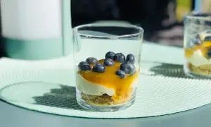 En läcker cheesecake i glas med blåbär och en gyllene sås. Perfekt för en solig sommardag.