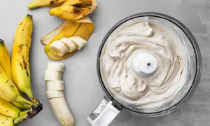 En matberedare fylld med krämig bananfrukt-glass bredvid skalade och skivade bananer.