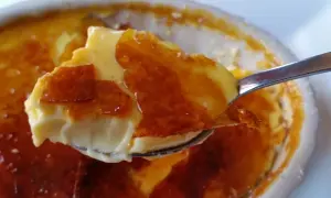 En sked lyfter en bit krämig creme brulee med knäckig yta.