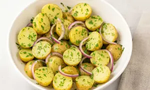 En skål med fransk potatissallad, full av små kokta potatisar, rödlök och färsk persilja.