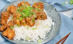 Krispig orange chicken med sesamfrön och salladslök serveras på en bädd av vitt ris. En läcker asiatisk rätt.