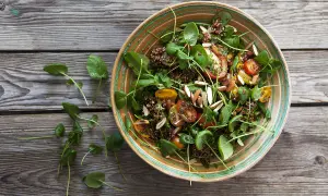 En härlig quinoa sallad med körsbärstomater, gröna blad och mandelspån, serverad i en vacker skål på en träbakgrund.