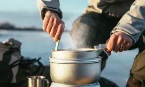 En person lagar mat på Trangia utomhus. Ånga stiger från kastrullen medan maten rörs om.
