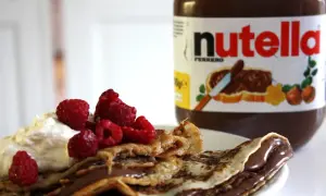 En pannkakstårta med nutella, grädde och hallon. En burk nutella syns i bakgrunden.