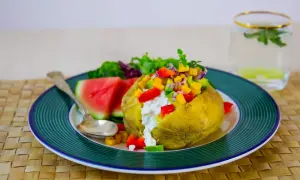 En saftig bakad potatis med en färgglad fyllning av grönsaker och en klick krämig ost. Serveras med vattenmelon och en frisk dryck.