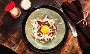 En läcker koreansk råbiff med en gul äggula i mitten, toppad med strimlad rättika och sesamfrön. Serveras på en vacker tallrik med en mörk servett och gaffel.