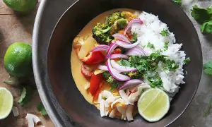 En skål med klimatsmart mat: ris, broccoli, paprika, rödlök och kokosflingor i en krämig currysås, toppad med lime och koriander.