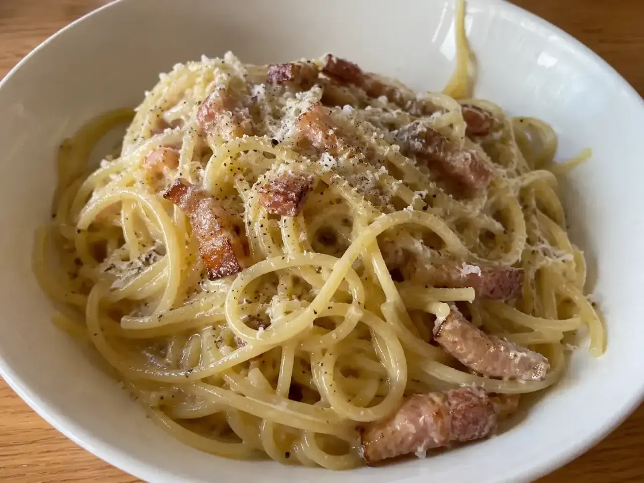 En skål med krämig pasta carbonara, toppad med parmesan och svartpeppar.
