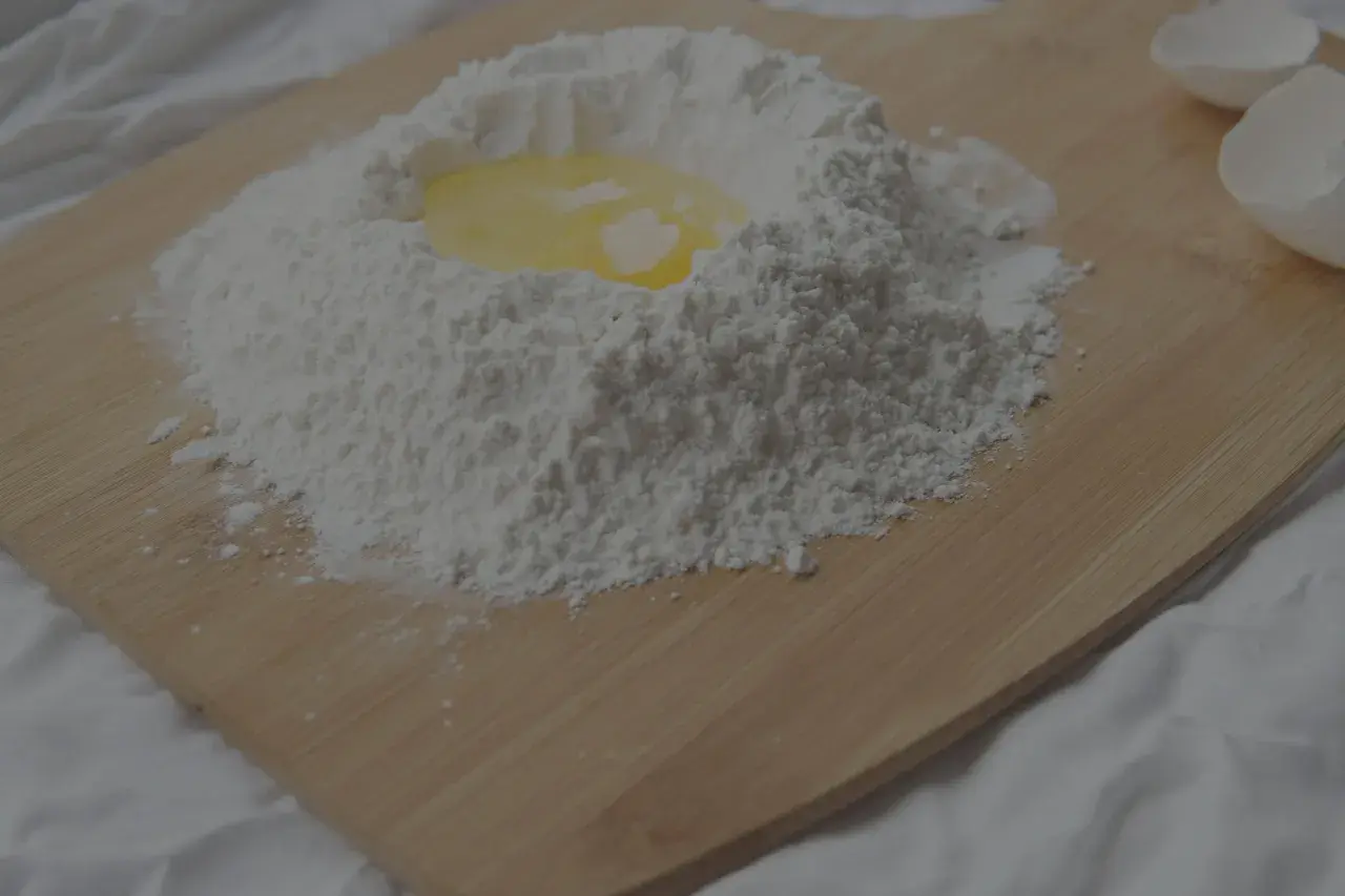 Mjöl och ett ägg ligger på en skärbräda, redo att blandas. Kanske för en kaka eller pannkakor, där bikarbonat och bakpulver kan komma till användning.