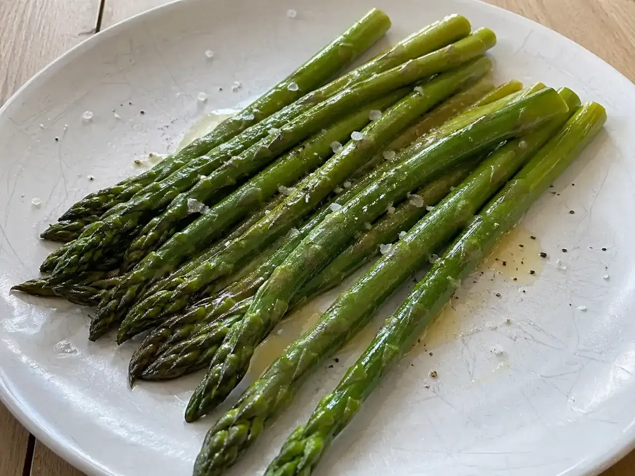En tallrik med perfekt kokt sparris, strödd med flingsalt och nymalen svartpeppar. Enkel och god matlagning.