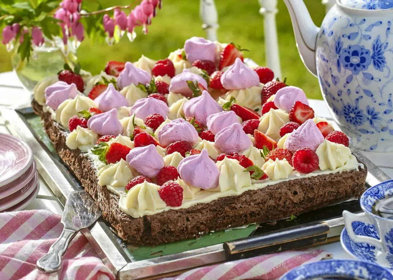 En chokladkaka i långpanna, dekorerad med grädde, maränger och färska bär. Perfekt för ett sommarfika.