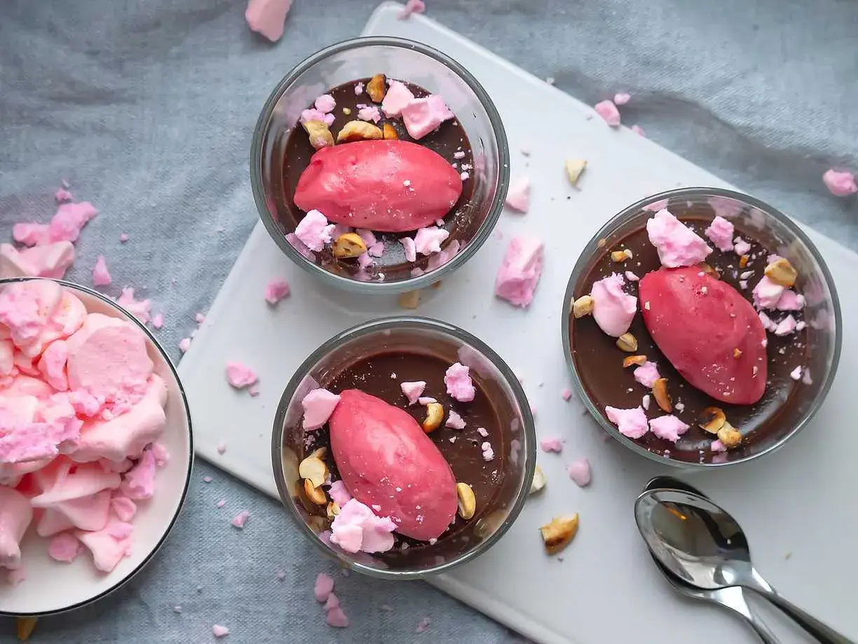 Tre glas med chokladmousse toppas med rosa sorbet, krossad maräng och nötter. Dessa goda desserter ser aptitliga ut!