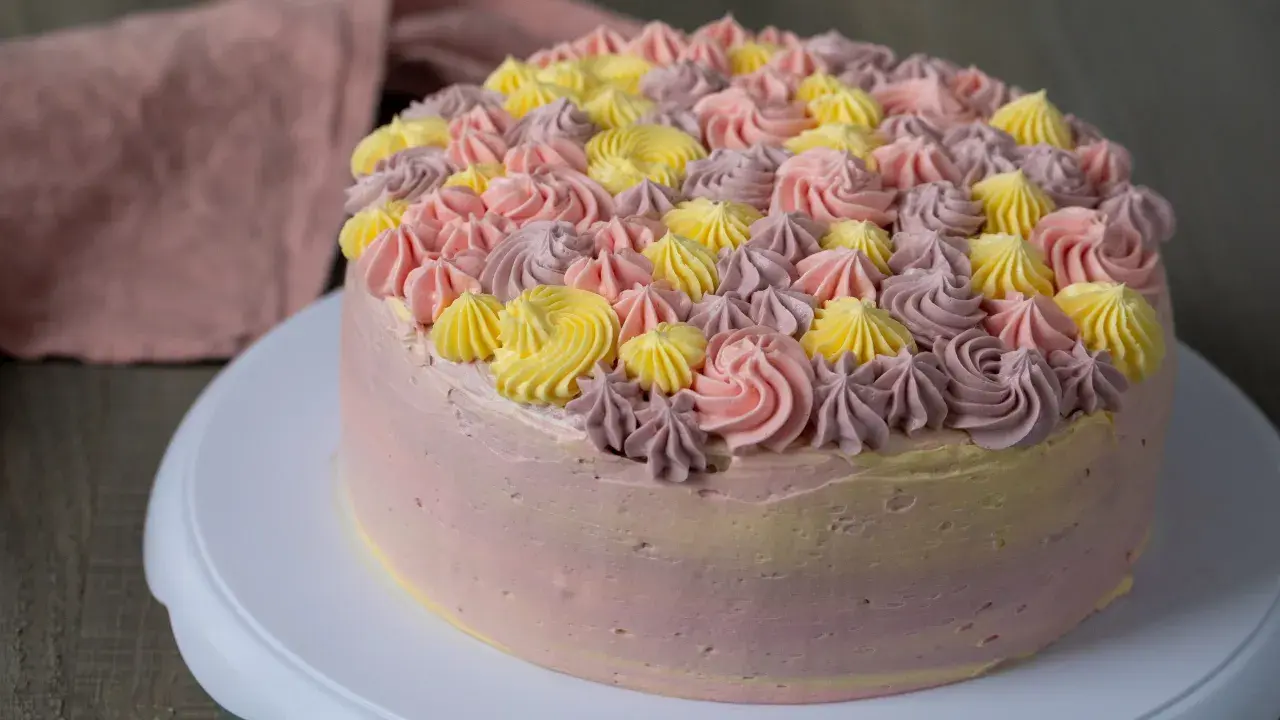 En vacker tårta med rosa, lila och gula frostingrosor. Denna tårta är perfekt för att spritsa tårta till ett speciellt tillfälle.