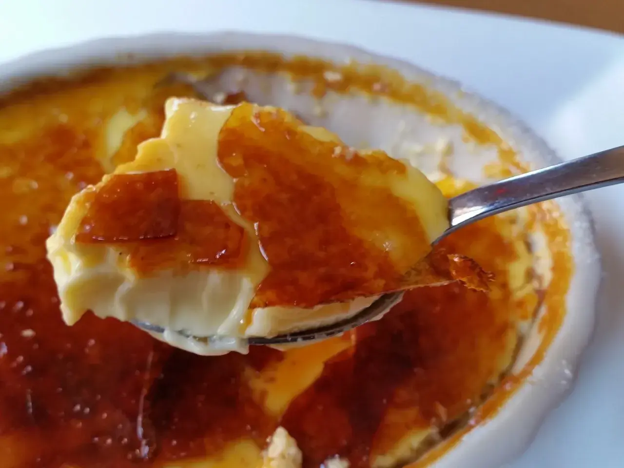 En sked lyfter en bit krämig creme brulee med knäckig yta.