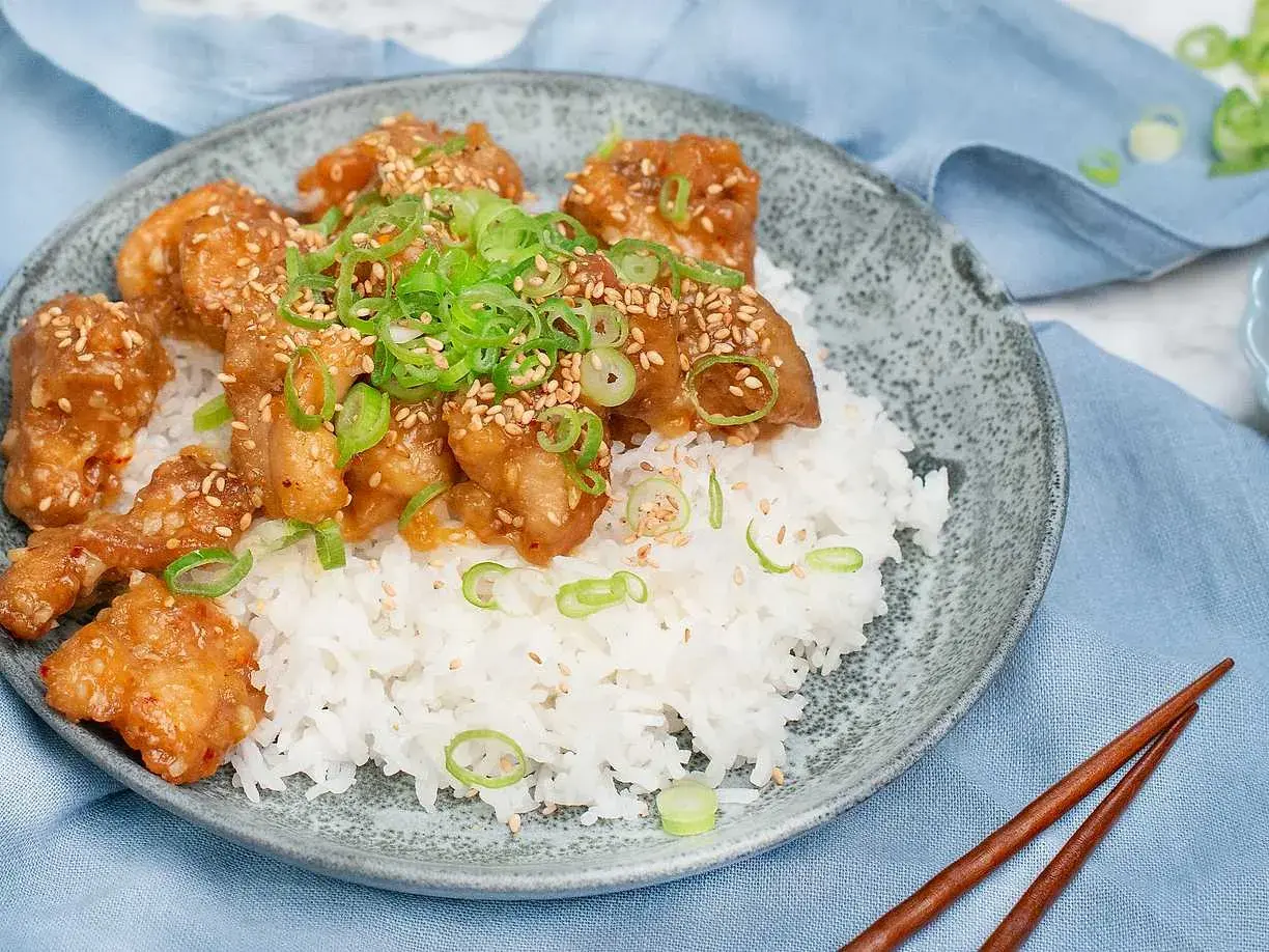 Krispig orange chicken med sesamfrön och salladslök serveras på en bädd av vitt ris. En läcker asiatisk rätt.