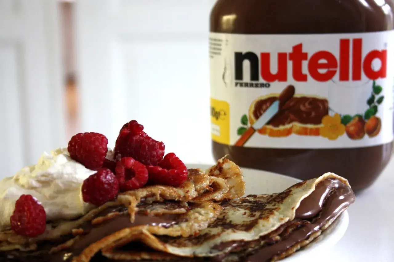 En pannkakstårta med nutella, grädde och hallon. En burk nutella syns i bakgrunden.