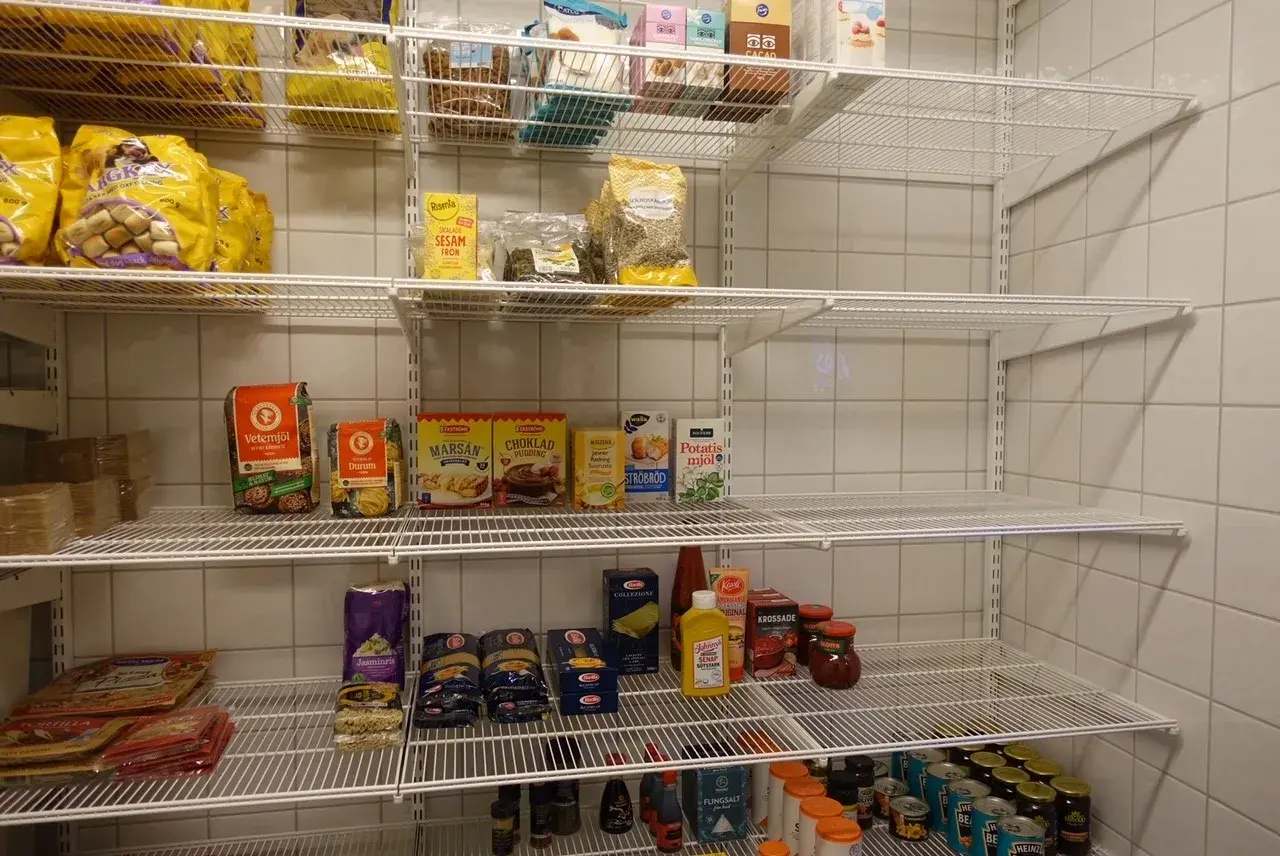 Hylla med basvaror att ha hemma: mjöl, pasta, krossade tomater, senap, sesamfrön och mer.