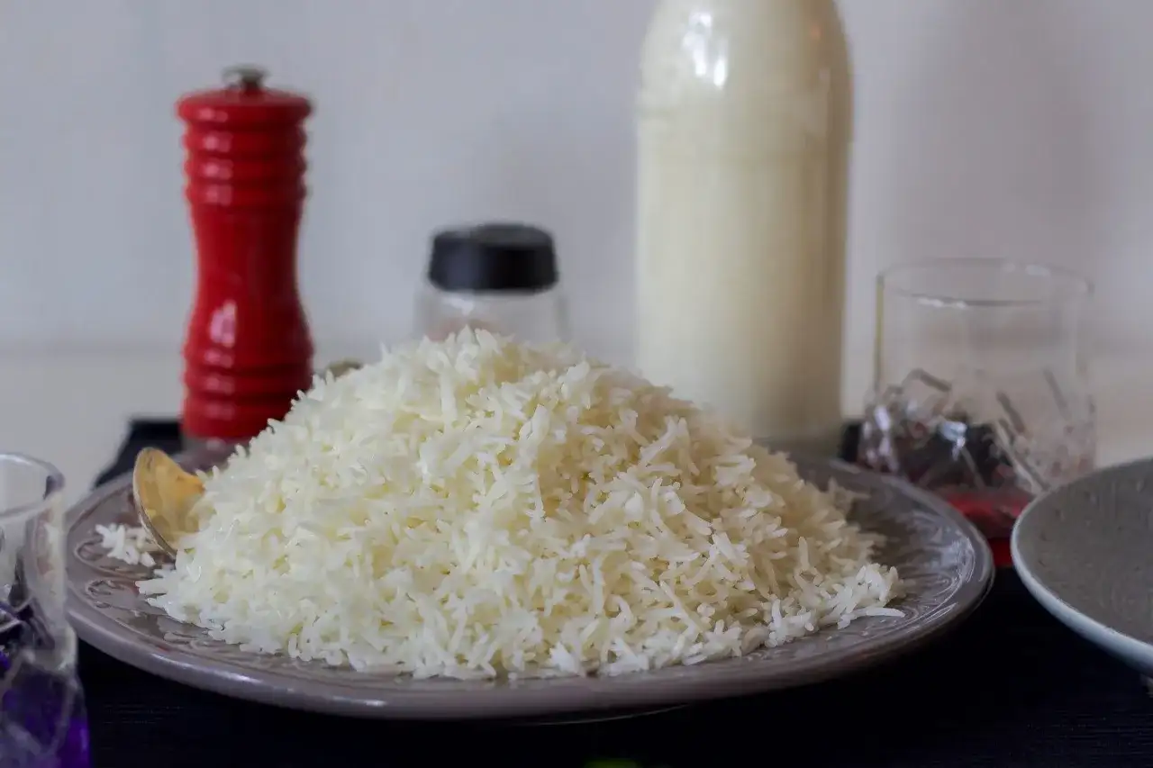 En stor hög med fluffigt ris, perfekt för att koka ris till en måltid. En röd pepparkvarn och en flaska mjölk står i bakgrunden.