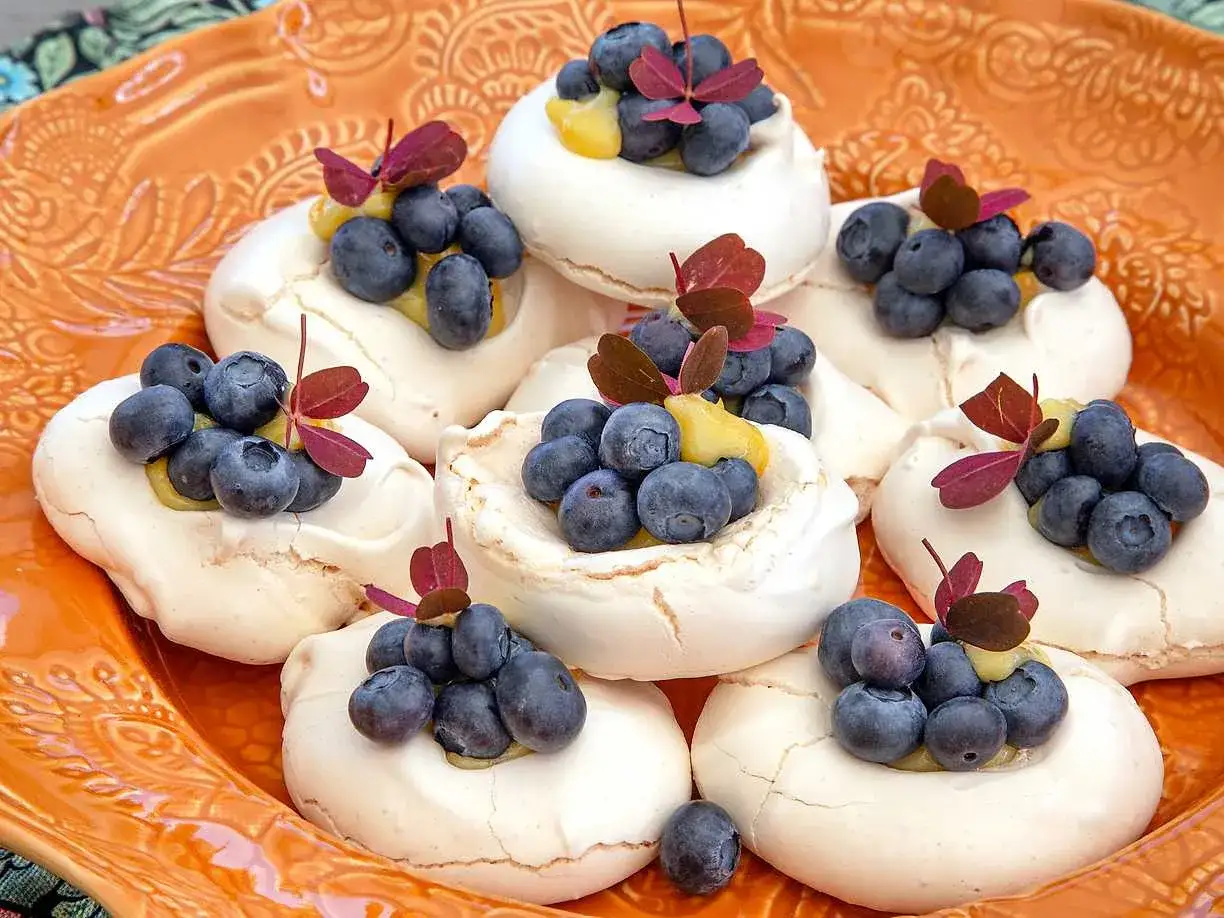 Små pavlovakakor med blåbär och citrongelé, dekorerade med röda blad. En festlig dessert!