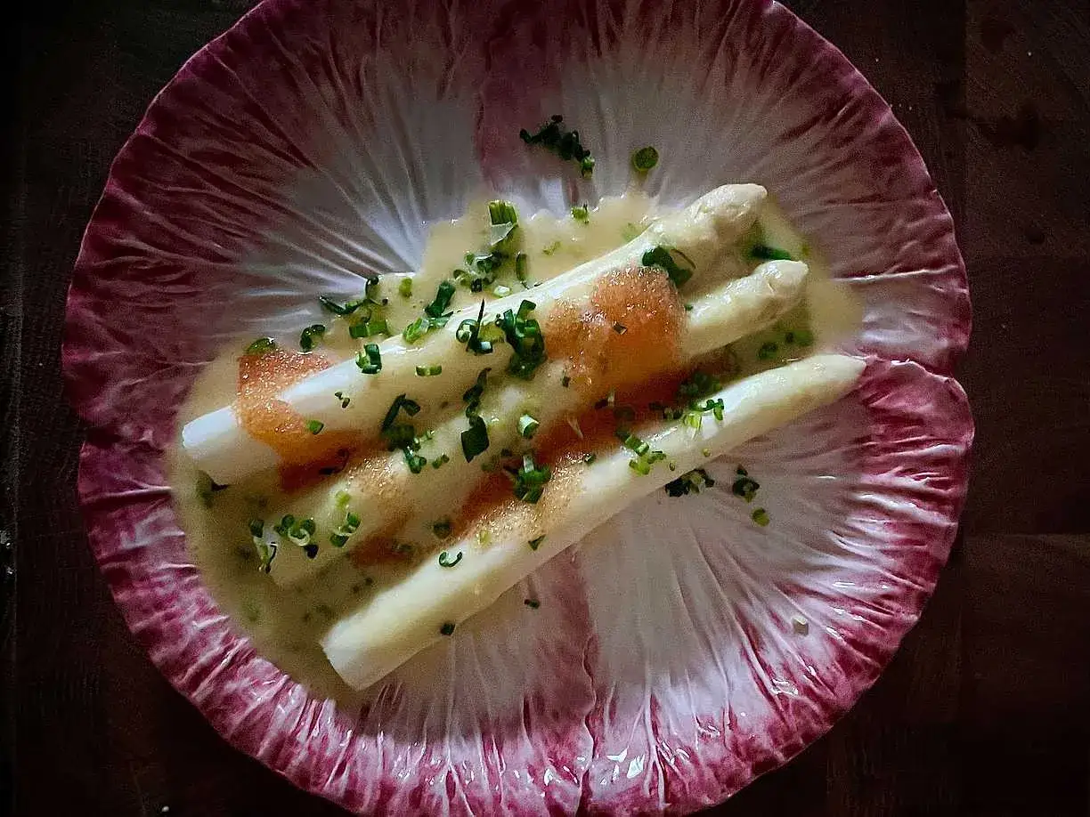 Vitt sparris, perfekt kokt, serveras i en krämig sås med kaviar och gräslök på ett rött endiveblad.