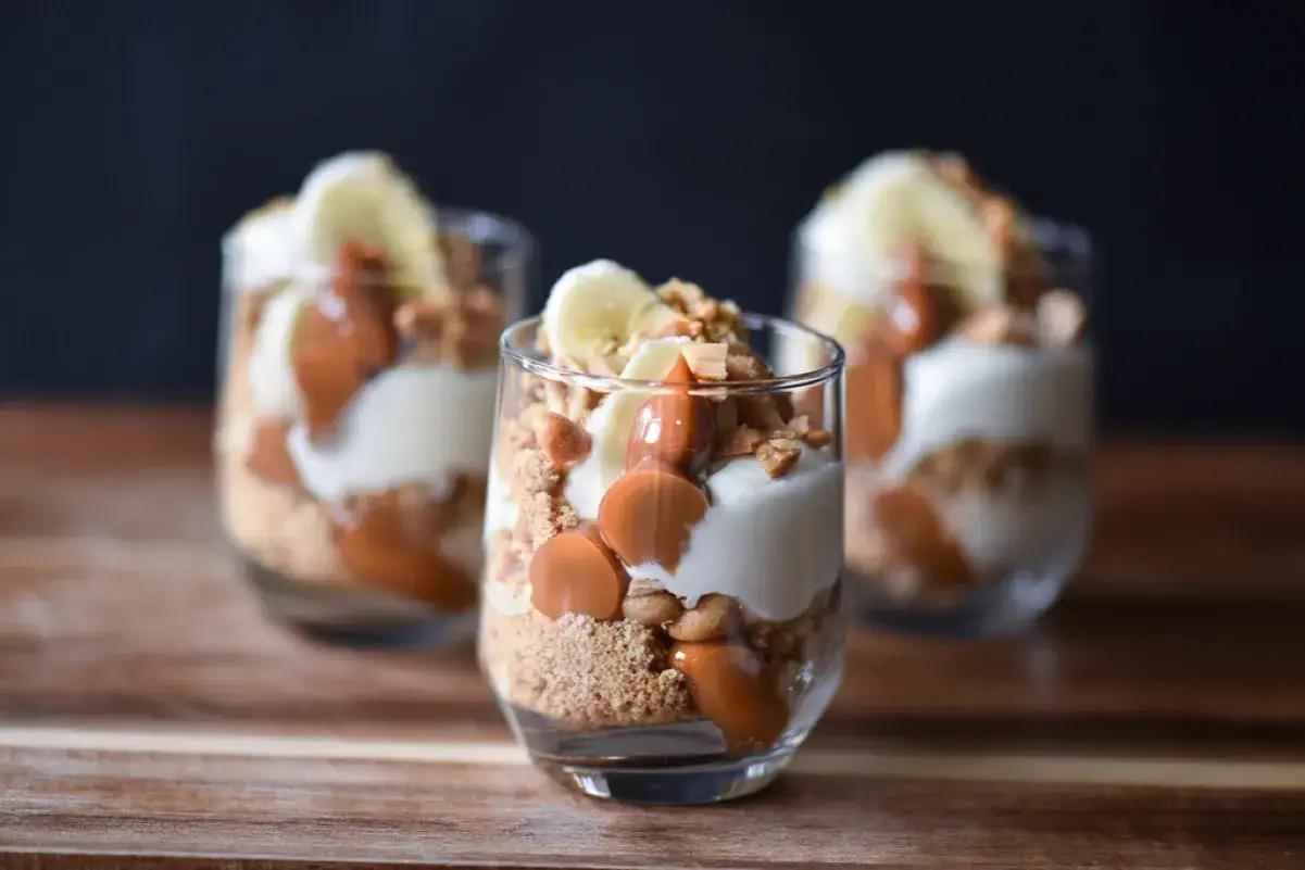 Tre läckra banoffee paj i glas med lager av kexsmulor, kolasås, grädde och banan.