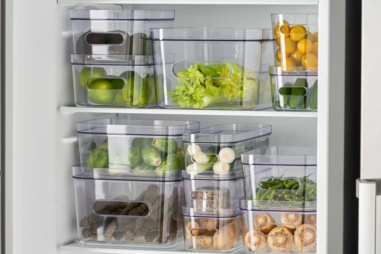 Genomskinliga förvaringslådor i kylen med grönsaker och frukt, som avokado, lime, selleri, brysselkål, sparris och tomater. Ett smart sätt att minska matsvinn.