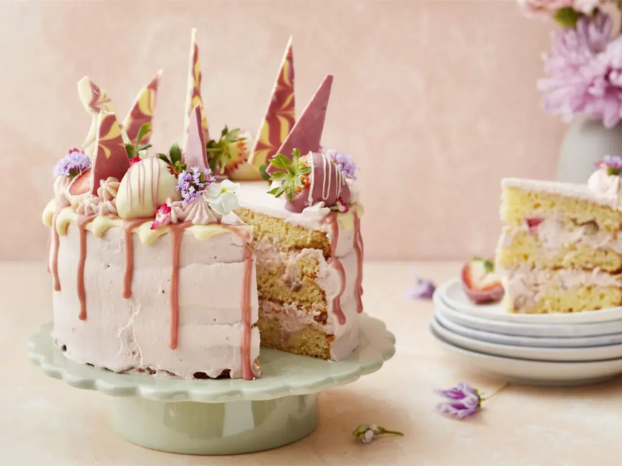 En vacker jordgubbstårta med rosa frosting, chokladdekorationer och blommor. En bit är uppskuren och visar de saftiga lagren. Perfekt för att spritsa tårta till ett speciellt tillfälle.